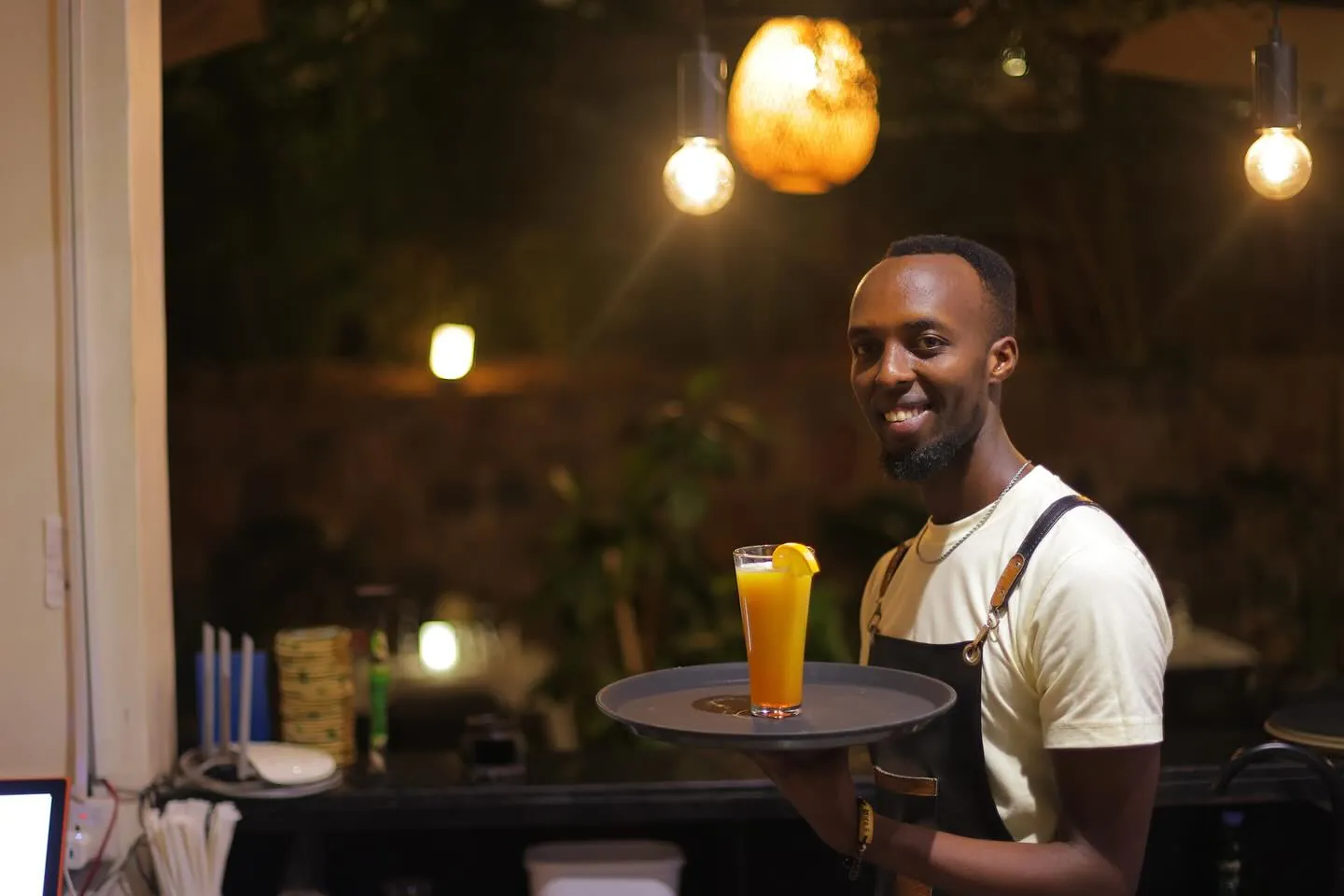 A member of the Kalih Villa team carrying a drink on a tray, warm lights behind