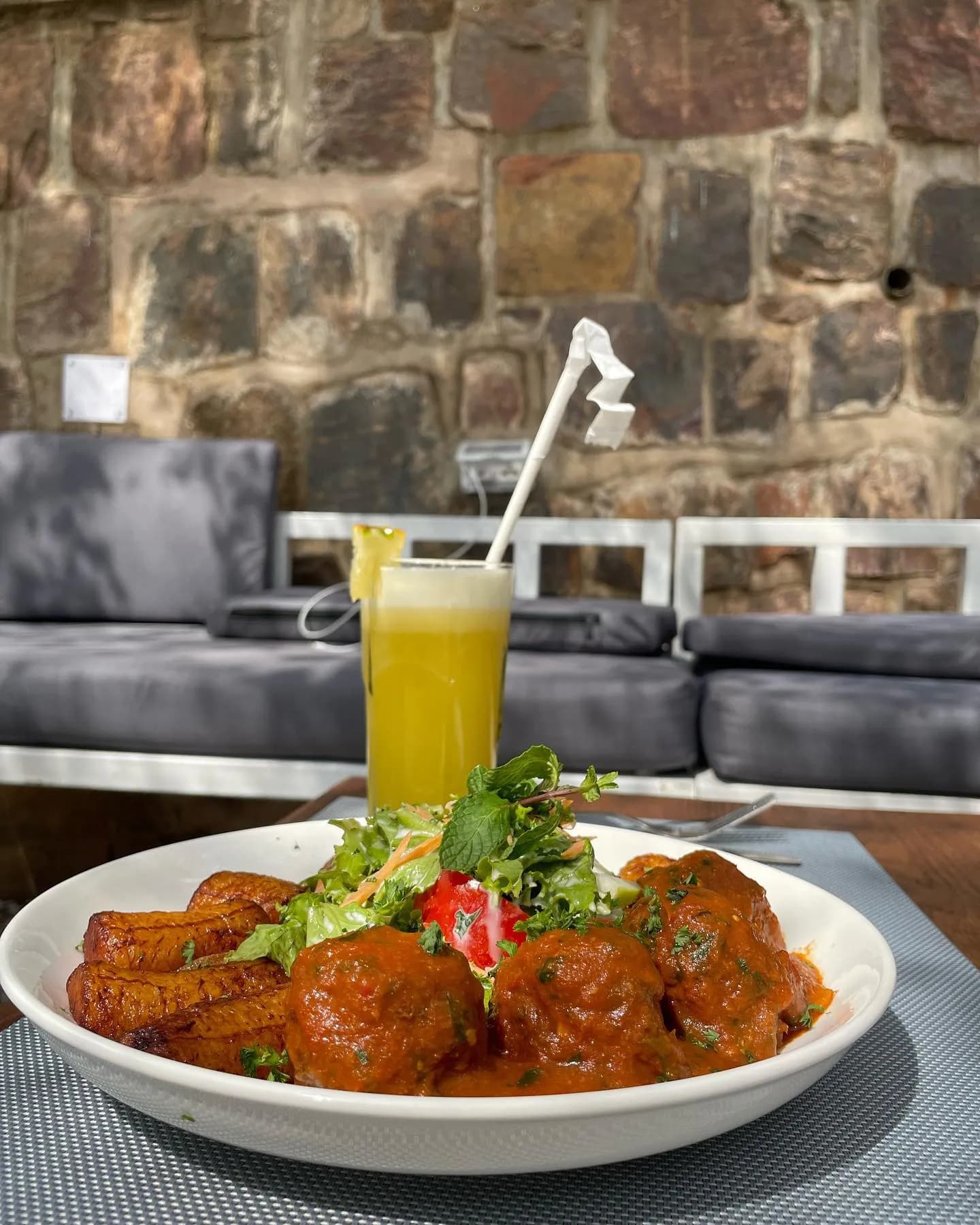 A plated main course and a fresh juice against a stone wall
